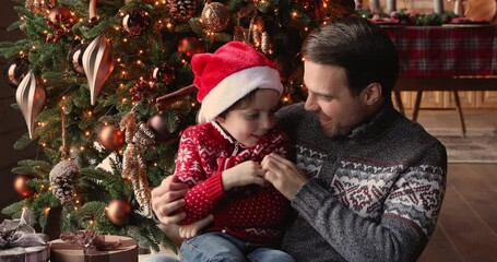 Dad tickle his preschool son sit near bright decorated with baubles and twinkle lights xmas tree enjoy time together play having fun on Christmas Eve at home. New Year celebration, x-mas mood concept