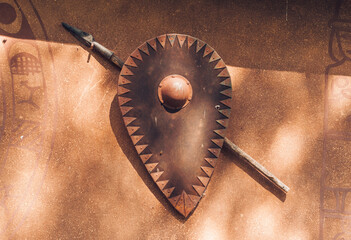 Scythian ancient spear and shield illuminated with sunshine on brown wall © Viktoriia