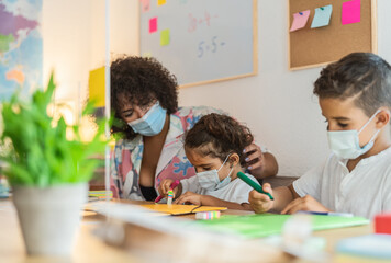 Fototapeta premium Teacher with children wearing face mask in preschool classroom during corona virus pandemic - Healthcare and education concept
