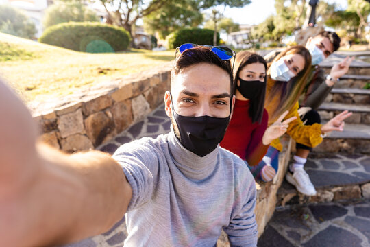 Outdoor group portrait of happy young people with medical mask - Millennial man take a selfie with his friends lined up behind him - New normal outdoor activity with Coronavirus pandemic