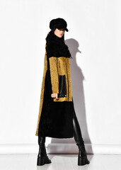 Stylish woman in fur cap two-tone karakul fur coat, leather pants and  shoes stands back to camera and turned