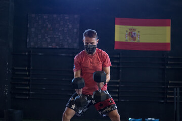 Chico con mascarilla en un gimnasio realizando Cross training con mancuernas