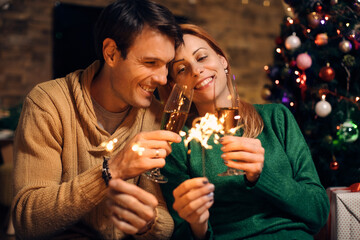 Happy couple using sparklers and toasting with Champagne on New Year's eve at home.