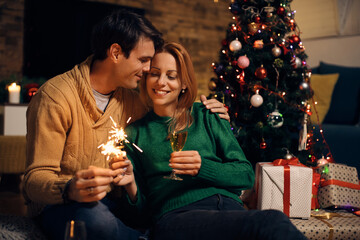 Loving couple celebrating Christmas eve with Champagne and sparkles at home.