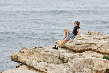 Girl sitting on rocks looking to the ocean. Side view