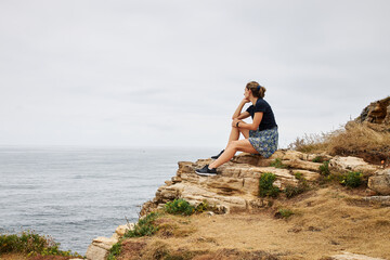 Girl sitting on rocks looking to the ocean