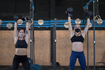 Chicas en un gimnasio con mascarilla realizando Cross training con mancuernas