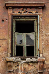 Old window with broken windowpane and weathered wooden frame on rough grungy textured wall