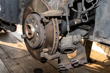 Disassembled front brake caliper on the car, which is on the car jack in the workshop.