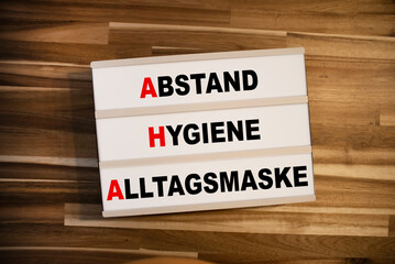 Light box or lightbox with the german acronym AHA - Abstand, Hygiene, Alltagsmaske on wooden background