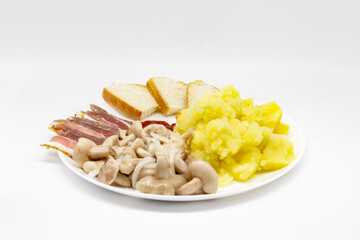 Pickled butter mushrooms with onions on a plate with bacon, potatoes and slices of bread isolated on a white background. Delicious Ukrainian meal for lunch or dinner.