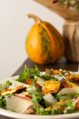 Light autumn salad with arugula, baked pumpkin, prosciutto and young parmesan, a plate of salad on a wooden table, chrysanthemums in a vase