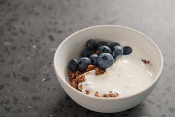 Healthy breakfast with whole grain granola and fresh blueberries in white bowl on concrete background