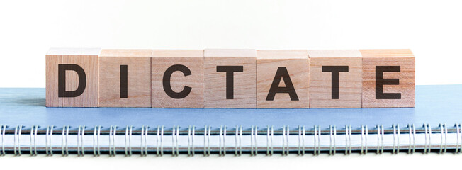 DICTATE - a word made of wooden blocks with black letters, a row of blocks is located on a blue Notepad.