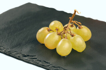 Branch of white grapes on black plate background