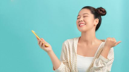 Joyous asian woman with big smile chatting using cell phone and showing thumb up isolated over...