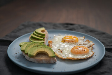 fried egg with two avocado sandwiches for breakfast on a blue plate