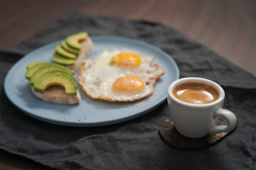 fried egg with two avocado sandwiches and espresso for breakfast on a blue plate