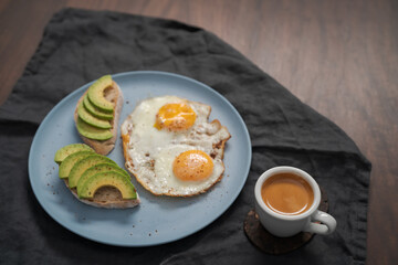 fried egg with two avocado sandwiches and espresso for breakfast on a blue plate