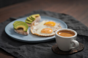 fried egg with two avocado sandwiches and espresso for breakfast on a blue plate