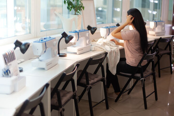 Beautiful woman tailor with long dark hair completing work with sewing machine at workplace