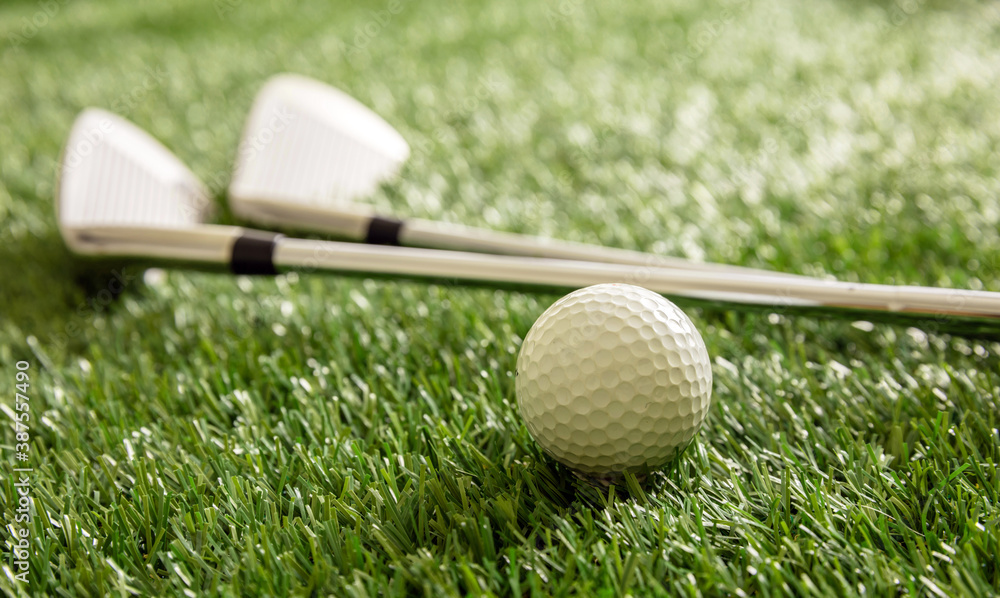 Wall mural Golf ball and sticks on green grass golf course, close up view.