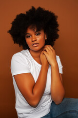 pretty young african american woman with curly hair posing cheerful gesturing on brown background, lifestyle people concept