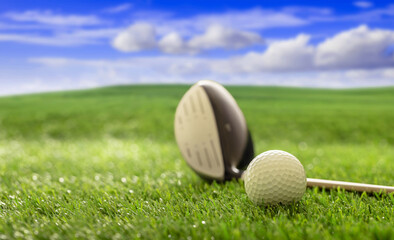 Golfball and stick on green grass golf course, blue cloudy sky background