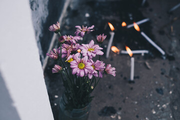 Aster flowers and lighted candles in front of the tomb during a visit to a dead family member's  grave. Selective focus.