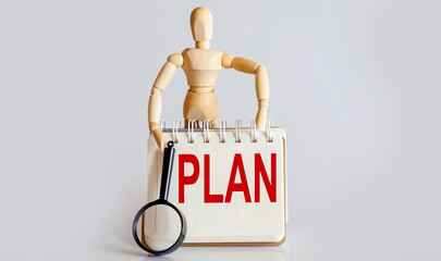 Wooden man shows with a hand to white notepad with text PLAN