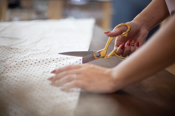 Well groomed woman hands cutting polka dot fabric with tailor scissors for sewing dress in studio