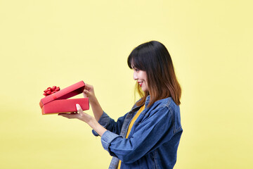 A beautiful excited young Asian woman in hand is opening a red gift