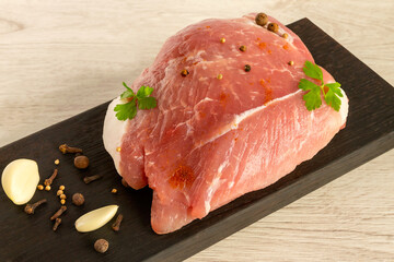 A raw piece of pork with spices on a black kitchen board.
