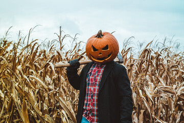 Scary Halloween man wearing a pumpkin head holds an axe on his shoulders. Landscape