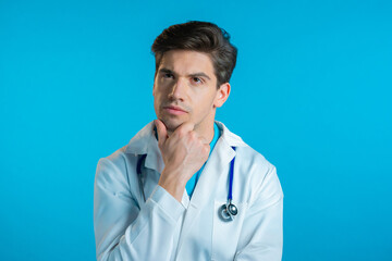 Thinking doctor man looking up and around on blue background. Worried contemplative face expressions. Handsome doc in medical coat with stethoscope