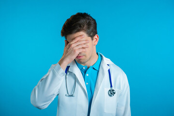 Frustrated doctor man in white wear over blue wall background. Doc is tired, bored of work, he...