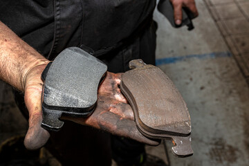A car mechanic holds in a dirty, open hand a new and old brake pad, visible brake lining of the...