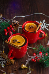 Fototapeta na wymiar Aromatic, hot and delicious mulled wine with orange, cinnamon, star anise and cloves in red cups with Christmas decor. Feeling of celebration and warmth at home, vertical aspect ratio.