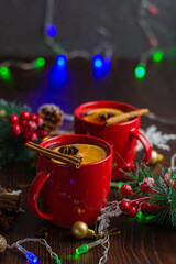 Aromatic, hot and delicious mulled wine with orange, cinnamon, star anise and cloves in red cups with Christmas decor. Feeling of celebration and warmth at home, vertical aspect ratio.