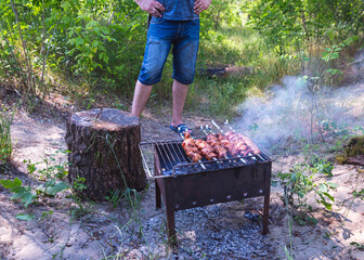 Man fries pork meat on the grill. Barbecue for a summer party. Skewers on a spit. Rest at nature.