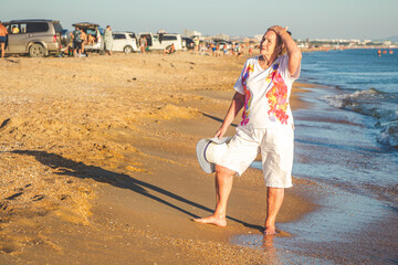 An elderly woman walks along the seashore. Summer vacation at the sea.