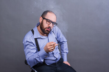 Armenian man with beard and braces smokes on gray background