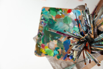 picking oil paintbrushes near canvas in workshop