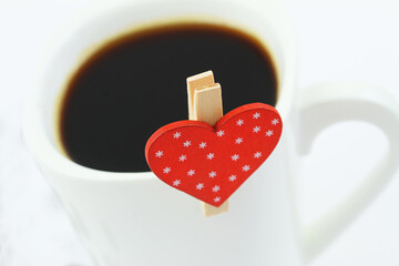 Close up of red heart attached to white mug with black coffee
