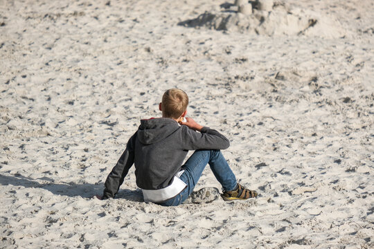 Ferien und Urlaub: Junge sitzt gemütlich in der Abendsonne am Strand im Sand und isst ein Eis