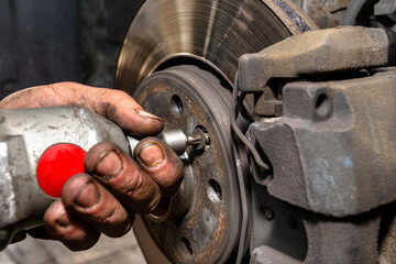 Unscrewing the old brake disc from the car with a pneumatic screwdriver.