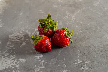 three fresh juicy strawberries lie on a concrete background.