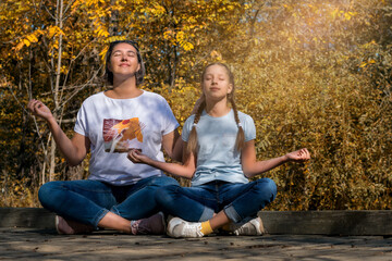 Happy mother and daughter meditate in nature, against the background of the autumn forest.