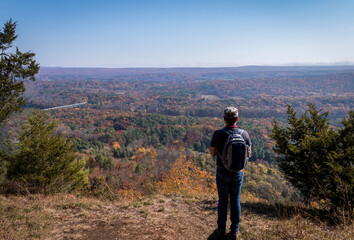 A lone man overlooks the Milford Bridge from a scenic point surrounded by brilliant fall foliage