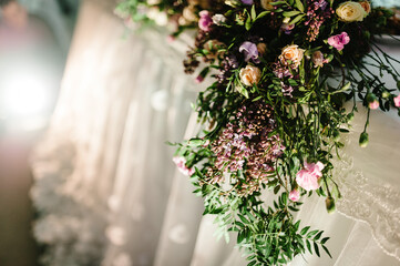 A composition of flowers and green is on a festive table at the wedding banquet hall. Close up.